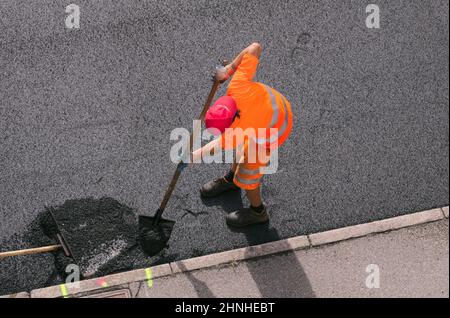 Asphaltarbeiter mit seiner Schaufel während des Straßenbelades Stockfoto