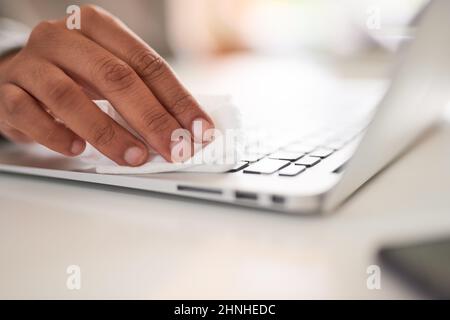 Ein Mann wischt seine Laptop-Tastatur ab, um sie von Keimen zu reinigen Stockfoto