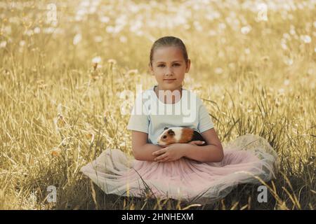 Mädchen mit Haustier in den Armen sitzt auf Gras. Stockfoto