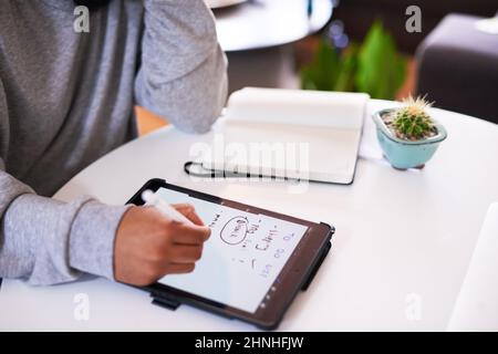 Eine über die Schulter gedrehte Aufnahme eines jungen Mannes, der auf einem Tablet schreibt Stockfoto