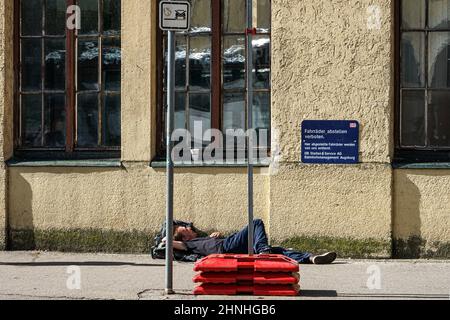 Ein betrunkener Mann, der auf dem Asphalt eines Bürgerwegs vor einer Station schläft. Stockfoto
