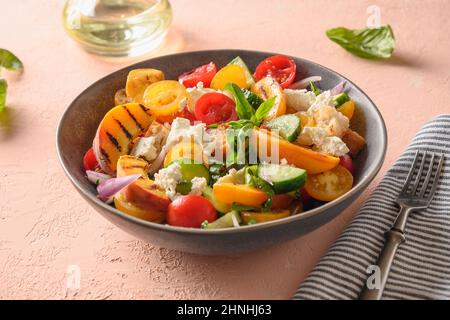 Panzanella-Salat mit Tomaten, Brot, Käse und gegrilltem Pfirsich. Nahaufnahme. Italienische Küche. Sommergemüse farbenfroher Salat. Stockfoto