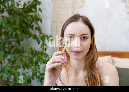 Junge Frau macht im Badezimmer eine Gesichtsmassage von Gua Sha. Gua Sha Jadestein zu Hause Behandlung Stockfoto