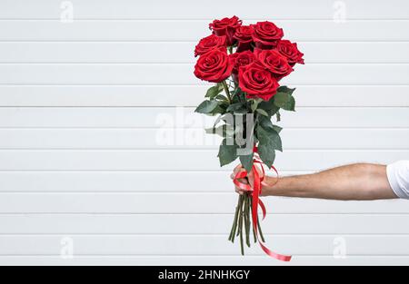 Blumenstrauß in der Hand auf hellem Hintergrund. Gentleman mit einem Strauß roter Rosen. Stockfoto