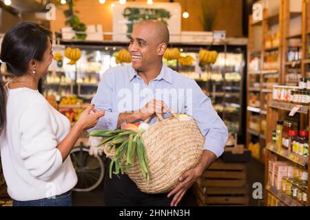 Fröhlicher hispanischer Mann, der im Supermarkt mit einer Freundin spricht Stockfoto