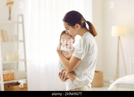 Glückliche, liebevolle junge Mutter hält und küsst ihr süßes, entzückendes kleines Kind Stockfoto