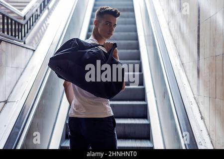Rückansicht eines jungen kaukasischen Mannes, der auf einer Rolltreppe am Flughafen auffährt. Stockfoto