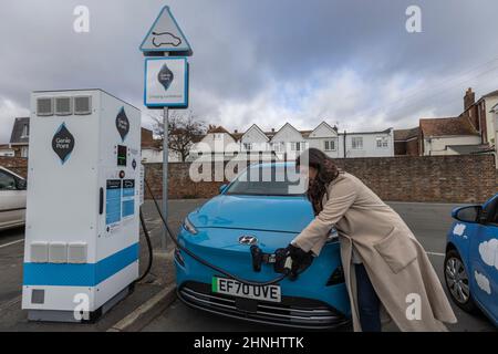 Dame mittleren Alters, die die Fahrzeugladestation „GeniePoint EV Charging“ in Hampshire, England, Großbritannien, verwendet Stockfoto