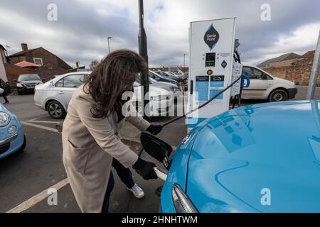 Dame mittleren Alters, die die Fahrzeugladestation „GeniePoint EV Charging“ in Hampshire, England, Großbritannien, verwendet Stockfoto
