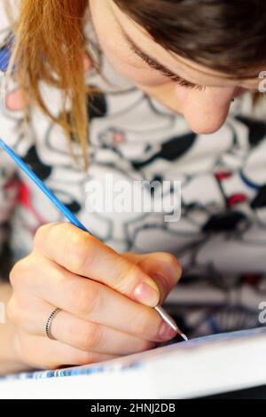Frau Hand hält einen Pinsel und malt mit Farbe, Malerei auf einer Staffelei zeichnet die Details des Bildes mit Farben. Selektiver Fokus. Vertikales Foto Stockfoto