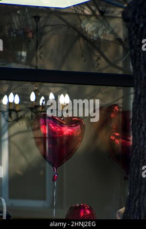 Roter Herzballon auf einem Schaufenster, um den Valentinstag zu feiern. Heller Kronleuchter im Hintergrund. Romantischer Tag der Liebe. Hochwertige Fotos Stockfoto