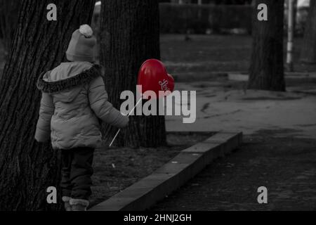 Schwarz-Weiß-Foto eines Kindes am Valentinstag mit einem roten Ballon mit Liebeszeichen. Romantischer Tag für Liebespaare. Hochwertige Fotos Stockfoto