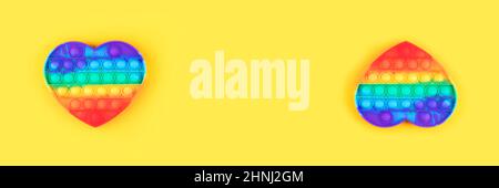 Banner aus Pop it Anti-Stress-Spielzeug in Form von Herz isoliert auf gelbem Hintergrund. Nahaufnahme. Stockfoto
