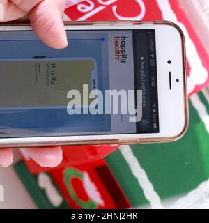 Tech Lifestyle - Nahansicht einer weiblichen Hand, die das Mobiltelefon hält und die Happify App auf dem Bildschirm anzeigt Stockfoto