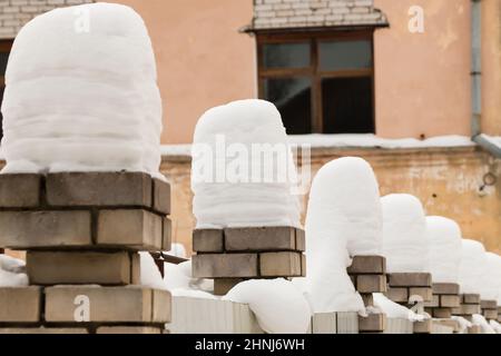 Hohe, wunderschöne Säulen aus weißem Schnee auf Ziegelsteinsäulen. Eine gerade Reihe kleiner Schneeverwehungen vor dem Hintergrund einer schäbigen Wand. Urbane Winterlandschaft. Wolkiger Wintertag, weiches Licht. Stockfoto