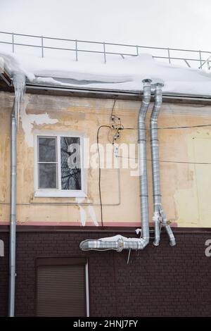 Zwei gebogene Auspuffrohre aus Metall an der Hauswand. Es liegt weißer Schnee auf der Oberfläche. Vor dem Hintergrund eines grauen Himmels. Wolkiger Wintertag, weiches Licht. Stockfoto