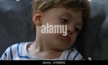 Ein schläfriger kleiner Junge, der sich auf dem Sofa niederlegt und sich auf den Schlaf vorbereitet Stockfoto