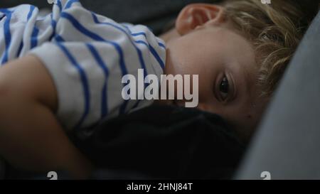 Ein schläfriger kleiner Junge, der sich auf dem Sofa niederlegt und sich auf den Schlaf vorbereitet Stockfoto