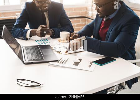 Zwei dunkelhäutige Partner eines afroamerikanischen Geschäftsmannes arbeiten bei einem Meeting auf einem Laptop im Büro. Erschwingliche private Kurse und Entfernung Stockfoto