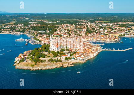 Das Adriatische Meer umgibt die Halbinsel mit der Stadt Rovinj mit dem Turm der Kirche der heiligen Euphemia. Rote Dächer von lokalen Häusern in der Nähe von Wäldern. Luftpanorama Stockfoto