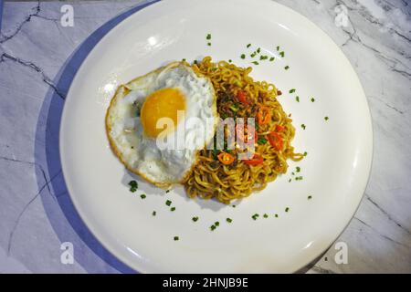 Leckere gebratene Nudel (Mie Goreng) mit Ei, Chili in Scheiben und gebratenen Zwiebeln. Serviert auf weißem Teller. Nahaufnahme von oben Stockfoto