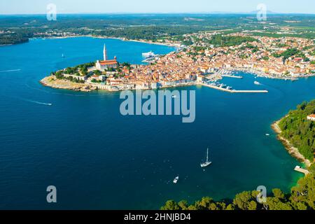 Umgebung von Rovinj Stadt mit St. Euphemia Kirche hohen Turm auf einem Hügel. Kroatische Stadthäuser von grünen Wäldern der Halbinsel umgeben. Luftpanorama Stockfoto