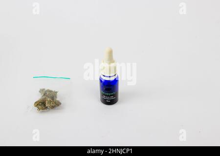 Nahaufnahme eines Grams trockener medizinischer Marihuanaknospen in einem durchsichtigen Plastikbeutel, blaue Glasflasche mit 10 ml CBD-Öl, Cannabisextrakt auf einem weißen Studio b Stockfoto