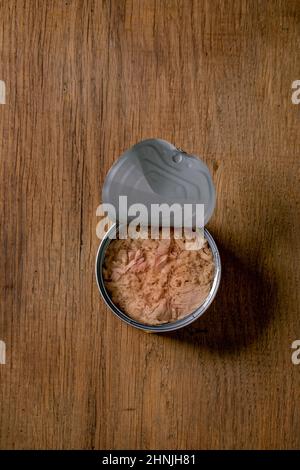 Thunfischkonserven in Öl in geöffneter Dose auf Holzboden. Draufsicht, Kopierbereich Stockfoto