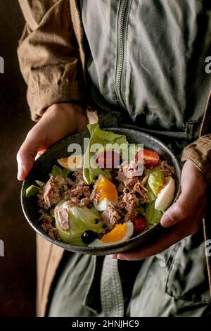 Frau hält in einer Schüssel mit Nicoise-Salat mit Thunfischkonserven, Oliven und Eiern. Omega 3 vegetarisches Gericht Stockfoto