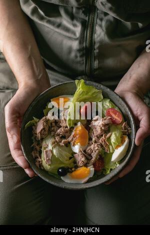 Frau hält in einer Schüssel mit Nicoise-Salat mit Thunfischkonserven, Oliven und Eiern. Omega 3 vegetarisches Gericht Stockfoto