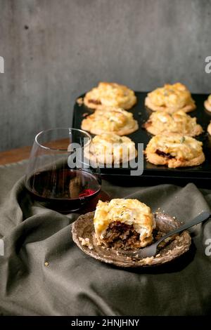 Ganze und beginnen zu essen hausgemachte Mince Fleisch traditionelle Mini-Kuchen mit Kartoffelpüree und Thymian in schwarzem Backblech und Glas Rotwein. Dunkle Linie Stockfoto