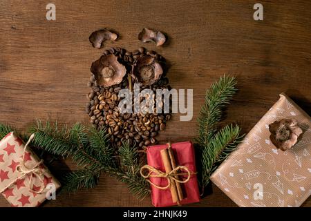 Eulenform aus Kaffeebohnen und Gewürzen. Eule sitzen auf Tannenweihnachtsbaum Zweig mit Kaffeetasse und Handwerk Geschenk-Boxen auf Holz Hintergrund. Witziger Myster Stockfoto