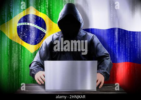 Anonymer Hacker, der an einem Laptop arbeitet, Flaggen von Brasilien und Russland Stockfoto