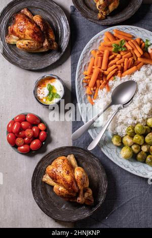 Esstisch mit gegrilltem Hähnchen, Reis und Gemüse gebackenen rosenkohl, Baby Karotte auf großen ovalen Teller und Gästetellern auf blauem Leinentischtuch o Stockfoto