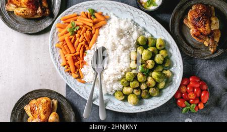 Esstisch mit gegrilltem Hähnchen, Reis und Gemüse gebackenen rosenkohl, Baby Karotte auf großen ovalen Teller in der Mitte und Gästetellern auf blauem Leinen ta Stockfoto