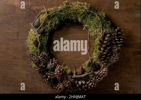 Handgefertigte DIY Handwerk Weihnachtsfeiertage Kranz mit natürlichen trendigen Wald Moos und Zapfen auf Holzhintergrund. Stockfoto