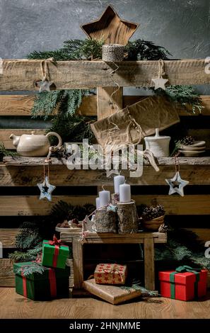 Weihnachtliche Mode rustikale Inneneinrichtung mit handwerklichem Holz, Keramik und Geschenkschachteln mit Adventskerzen auf alten Holzpaletten-Regalen als Hintergrund. Stockfoto