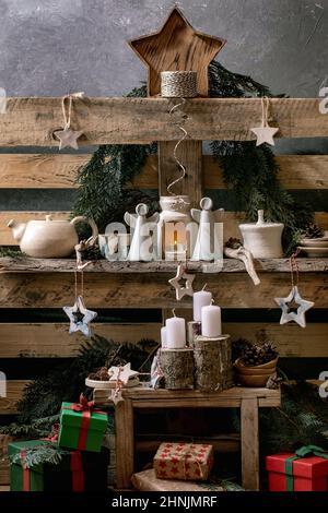 Weihnachtliche Mode rustikale Inneneinrichtung mit handwerklichem Holz, Keramik, Engel und Geschenkschachteln mit Adventskerzen auf alten Holzpaletten-Regalen als Bac Stockfoto