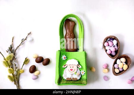 Ostern Grußkarte mit Schokolade Süßigkeiten Kaninchen in grüner Tasche, Süßigkeiten und Eier, Weidenzweige auf weißem Hintergrund. Osterfreuden Stockfoto