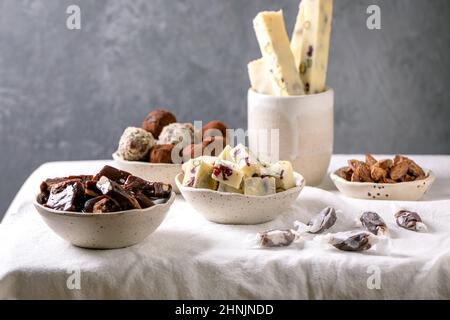 Auswahl an hausgemachten Schokoladen-Mandelnüssen aus Toffee, dunkler Schokolade-Trüffel, weißer Schokolade-Süßigkeitenbar in Schüsseln auf weißem Leinentischtuch. Handmad Stockfoto