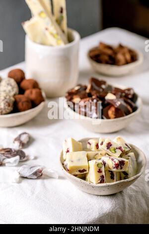 Auswahl an hausgemachten Schokoladen-Mandelnüssen aus Toffee, dunkler Schokolade-Trüffel, weißer Schokolade-Süßigkeitenbar in Schüsseln auf weißem Leinentischtuch. Handmad Stockfoto