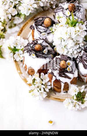 Hausgemachte traditionelle Ostern kulich Kuchen mit Schokolade Nester und Eier, blühende Kirschzweige auf weißem Marmor Hintergrund. Traditionelle ortodox EA Stockfoto