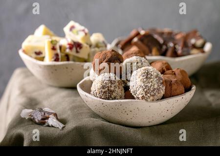 Auswahl an hausgemachten Schokoladen-Mandelnüssen aus Toffee, dunkler Schokoladentrüffel, weißer Schokoladen-Schokoriegel in Schüsseln auf grünem Leinentischtuch. Handmad Stockfoto