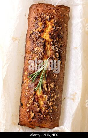Ganzer hausgemachter Zitronenkuchen mit Nüssen und Rosmarin auf zerknittertem Backpapier. Flach liegend, Nahaufnahme Stockfoto
