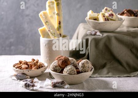 Sammlung von hausgemachten Toffee Schokolade Mandelnüsse Süßigkeiten, dunkle Schokolade Trüffel, weiße Schokolade Süßigkeiten Bar in Schalen auf weißem Leinen Tischtuch. Hand Stockfoto