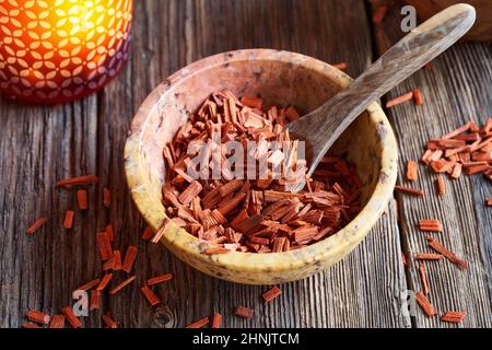 Rote Sandelholz-Chips in einer Schüssel mit einem Löffel, mit einer Duftlampe im Hintergrund Stockfoto