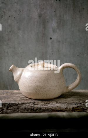 Craft weiß gesprenkelt handgemachte Keramik Teekocher für Teezeremonie stehen auf alten Holzregal mit grauen Wand im Hintergrund Stockfoto
