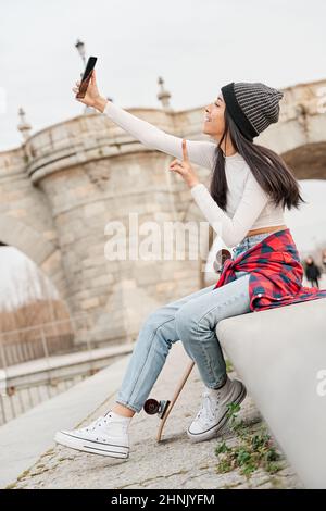 Selfie einer jungen Latina, während sie lächelt und mit ihren Fingern das Friedenszeichen macht. Stockfoto