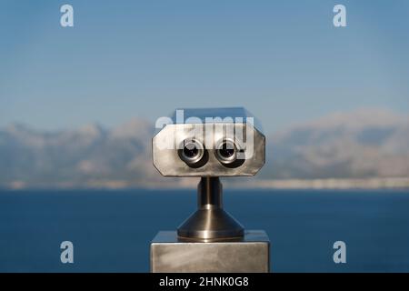 Münzferngläser vor Bergen und Meer Stockfoto