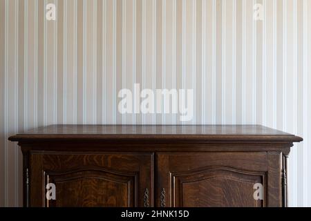 Vorderansicht Nahaufnahme eines leeren braunen Holzschranks mit Vintage-Schubladen an einer weißen Wand mit beigefarbenen Streifen Stockfoto